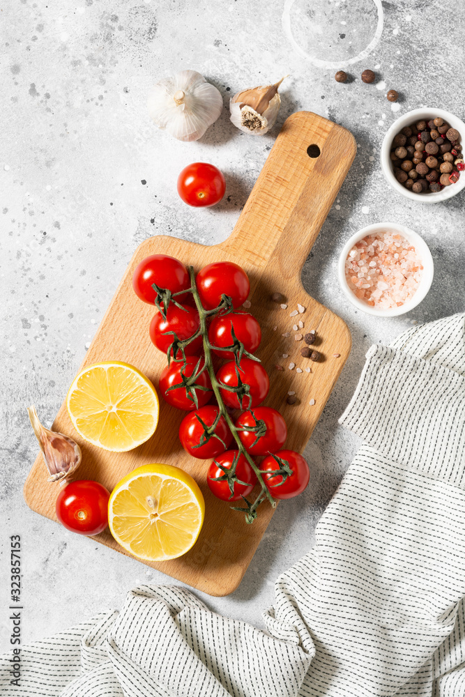 Cherry tomatoes on a wooden Board surrounded by spices, parsley and lemon on a light gray background. The view from the top
