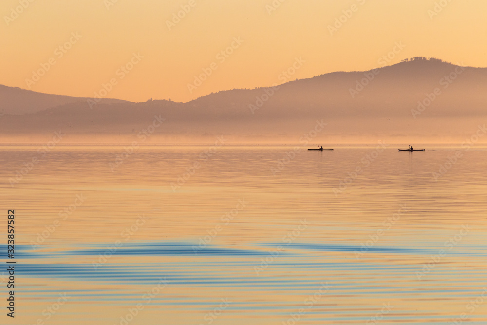 Beautiful view of a lake at sunset, with orange tones and two men on canoes