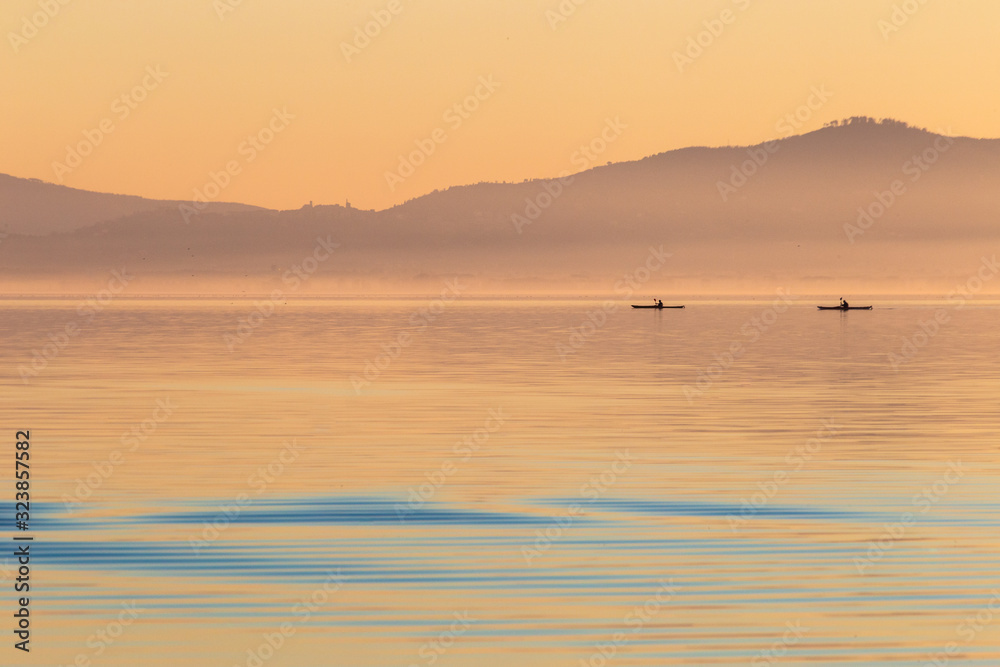 Beautiful view of a lake at sunset, with orange tones and two men on canoes Beautiful view of a lake at sunset, with orange tones and two men on canoes