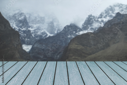 Dark tone of blue wooden planks table for product display template against blurred misty nature snow capped Karakoram mountain range landscape in Hunza valley. Gilgit Baltistan, Pakistan.