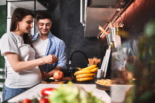 Smiling beautiful pregnant woman and man in the kitchen drink coffee and cook. Waiting for a new life, pregnancy.