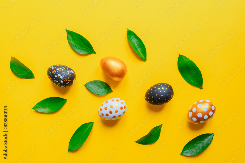 Festive easter background. Golden, black and white stylish pinted eggs with leaves on yellow background. Festive easter background. Golden, black and white stylish pinted eggs with leaves on yellow background.