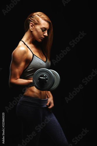 Young fit woman in sports equipment with dumbbells in her hands, sports embossed female body, black background, hard light. Copy space, sports banner