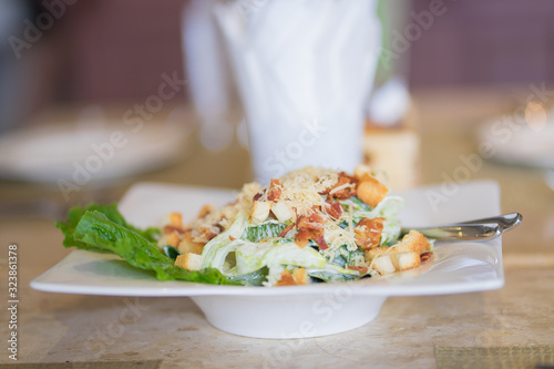 Caesar salad on designed white glass bowl  vegetable,cheese and crispy bread on top on mable dinner table 