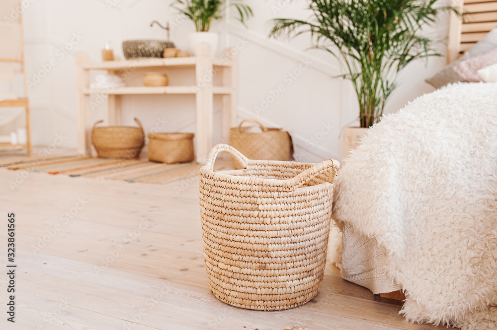 Light interior made of natural ecoy components. Wicker straw basket for storing clothes and things on the background of the washbasin and bath in the Boho style with wicker baskets and wooden shelves