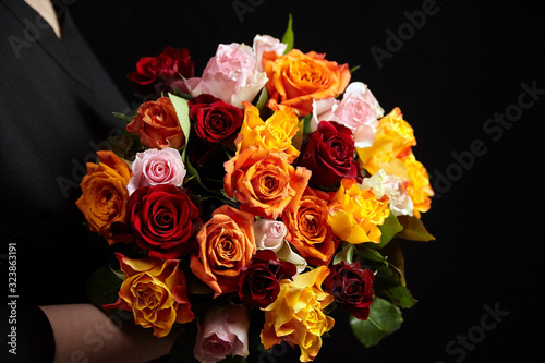 Bouquet of different color roses in female hand on a black background. Red, orange and pink flowers. Romantic Valentine's Day Gift