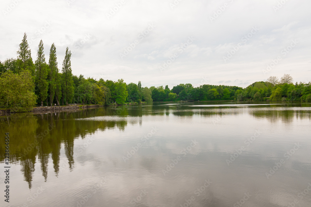 Beautiful lake during the fall season, Flers, Normandy, France. Green foliage in the background that reflects in the water. Cloudy day in the park.