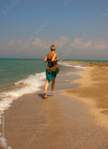 a young girl runs barefoot along the seashore. Summer, sea, sun, beach.