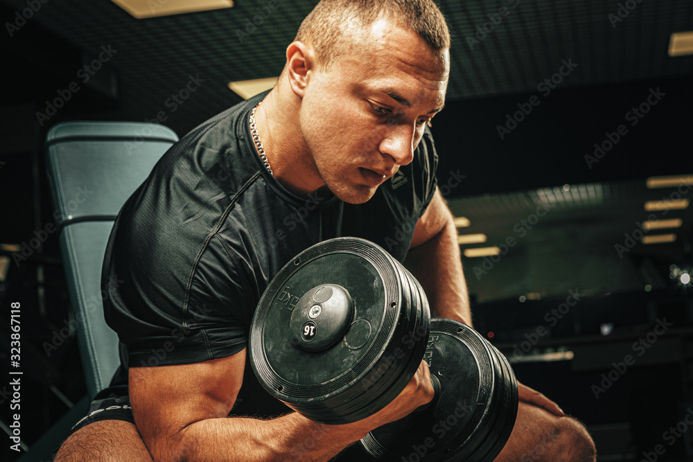 Muscular young man lifting weights in a dark gym Muscular young man lifting weights in a dark gym