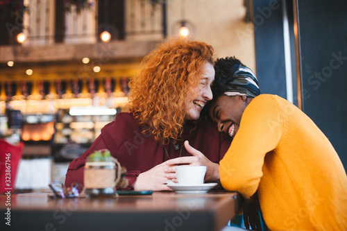 Two female friends laughing out loud in a cafe, having a good time.