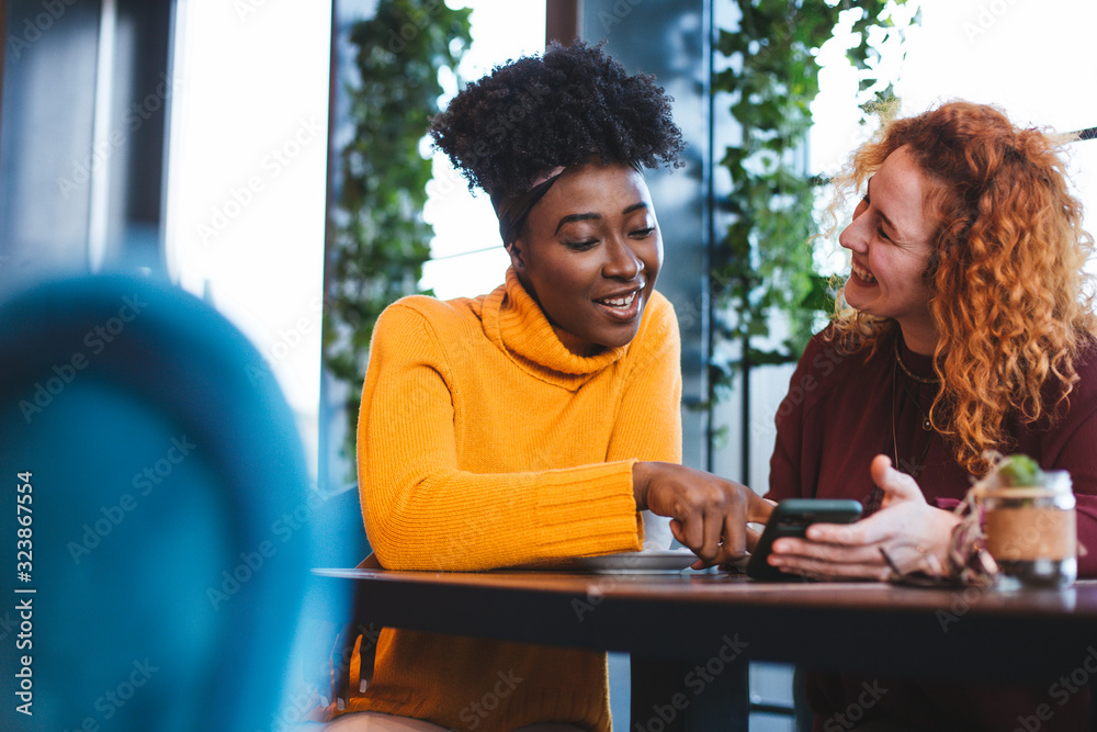© Sanja - Two female friends hanging out in a cafe, looking at the phone.
