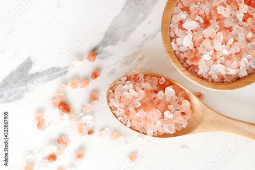 top view of himalayan pink rock salt in wooden bowl and spoon on white marble table.