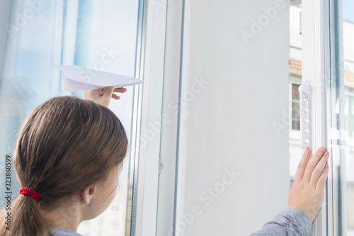 side view of a girl opening a window and wants to launch an airplane made of paper