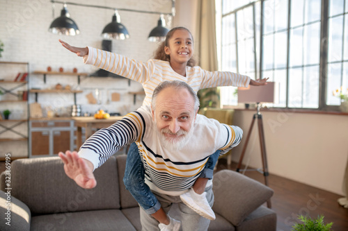 Bearded grey-haired man having fun with his dark-skinned granddaughter