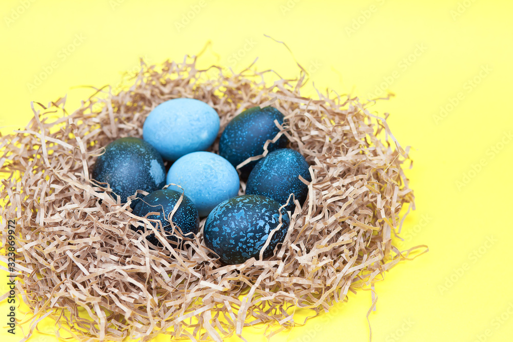Beautiful dark colored Easter eggs lie in a nest on a yellow background