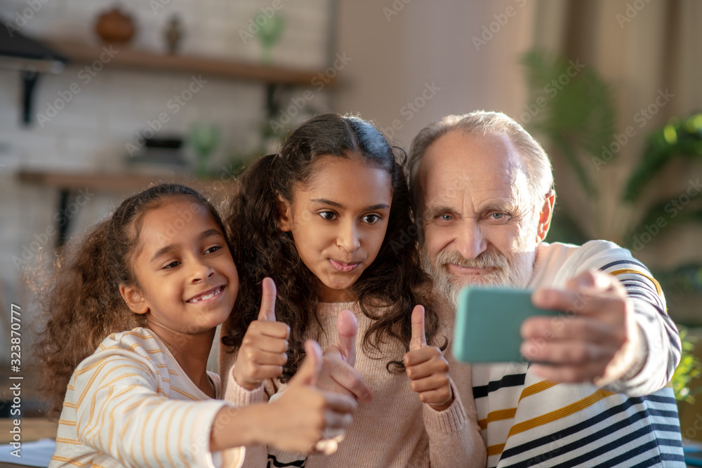 Fototapeta premium Grey-haired bearded man and his granddaughters making selfie