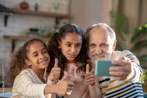 Grey-haired bearded man and his granddaughters making selfie