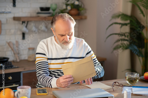 Bearded grey-haired man sitting at the table with a newspapaer in his hands