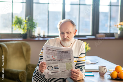 Quadro em tela Grey-haired bearded man in striped sweater looking distrustful