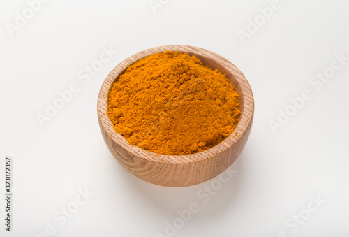 Turmeric powder in wooden bowl of curcuma root on white