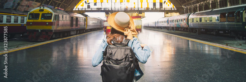Close up portrait back young woman backpacker in jeans jacket and straw hat standing in front of trains at train station