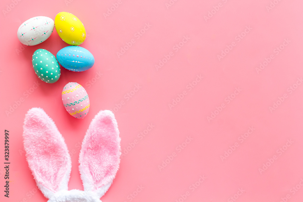 Easter symbols. Bunny and painted eggs on grass on pink background top-down frame copy space