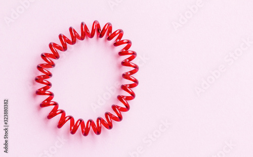 Red spiral rubber bands for hair on a pink background close-up, copy space for text