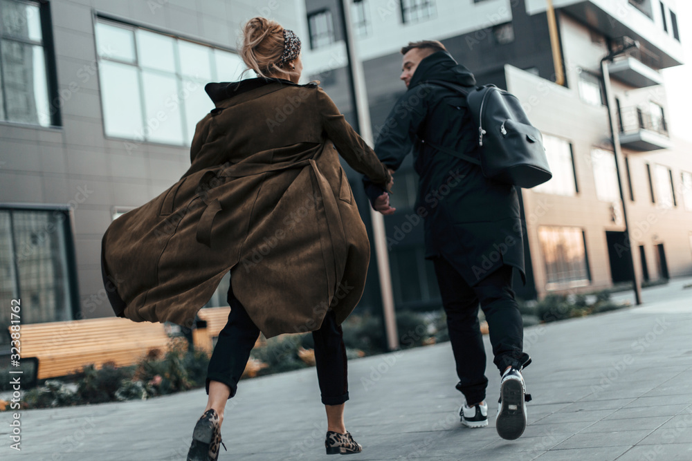 Back view of beautiful and young love couple holding hands and walking running on the road of urban city. Photo in motion Back view of beautiful and young love couple holding hands and walking running on the road of urban city. Photo in motion
