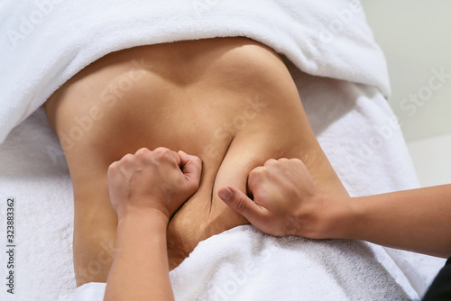 Masseur pulls hand the skin on the abdomen, showing the body fat in the abdominal area and sides. Treatment and disposal of excess weight, the deposition of subcutaneous fat.