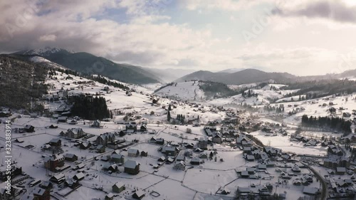 Aerial footage of small mountain village in winter time during sunny day with epic clouds photo