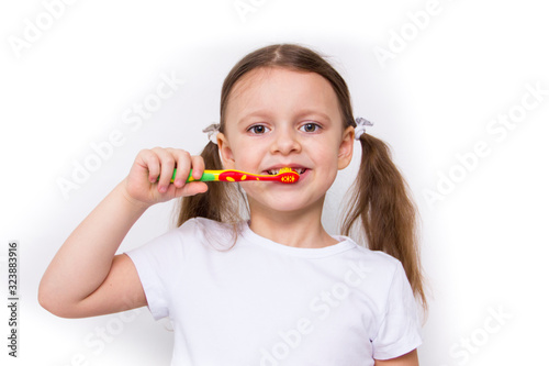 Cute smiling little girl in white T-shirt brushing her teeth with a colored toothbrush isolated on white background.