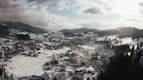 Aerial footage of small mountain village in winter time during sunny day with epic clouds photo