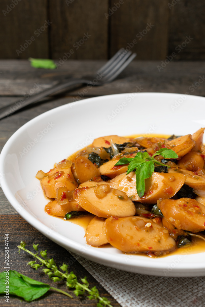 Fried basil with sausages in white dish on the old wooden table. Fried basil with sausages in white dish on the old wooden table.
