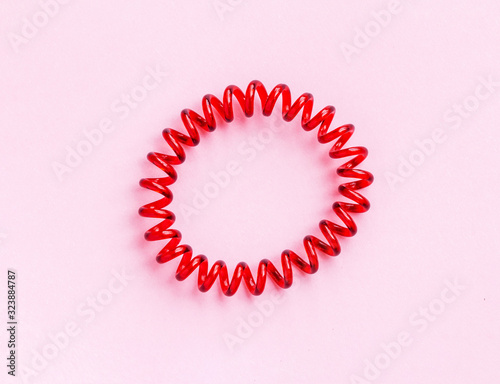 Red spiral rubber bands for hair on a pink background close-up