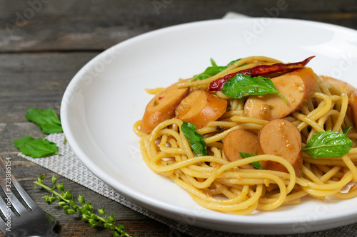 Spaghetti with sausages and fried basil in white dish on the old wooden table.
