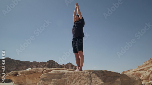 Handsome male staying in tadasana doing namaste on a rock in desert photo