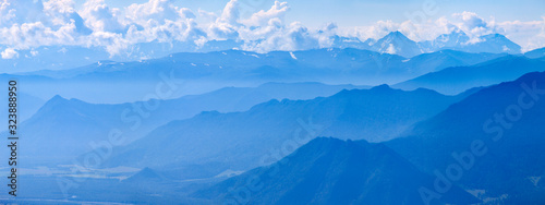 Mountains in blue haze, panoramic view. Peaks in the clouds, valley and mountainsides.