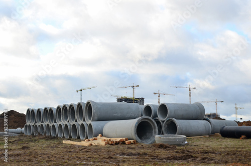 The drainage pipes at the large scale construction site against tower cranes and blue sky. Construction of high-rise buildings. Installation of water main, sanitary sewer, storm drain systems.