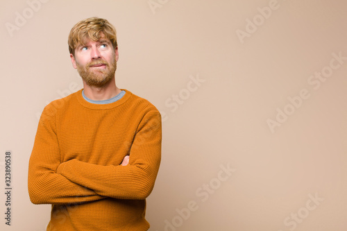 Foto young blonde man doubting or thinking, biting lip and feeling insecure and nervo