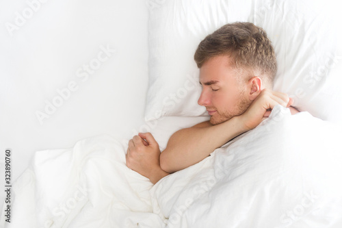 Happy handsome guy, young man is sleeping, having good dreams, smiling, lying on white pillow, covering with blanket. Copy space, top view. Healthy well sleep, daily regime, relaxation, rest concept.