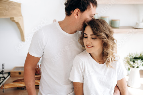 Close up portrait of an attractive couple in love in white t-shirts gently hugging in the kitchen