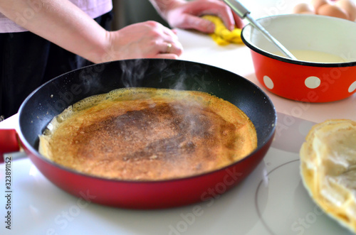 Cooking thin dairy pancakes in a frying pan on an electric stove, Shrovetide