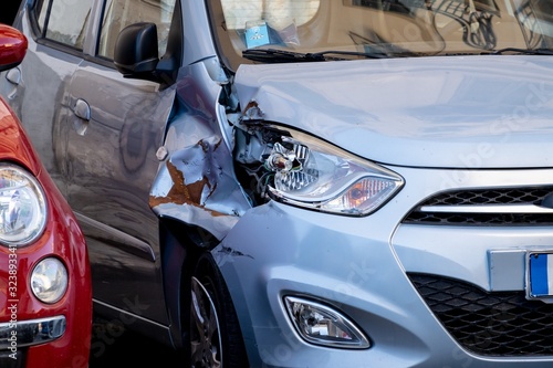 A small blue hatchback damaged in a car accident with a broken headlamp and fender waiting for repair
