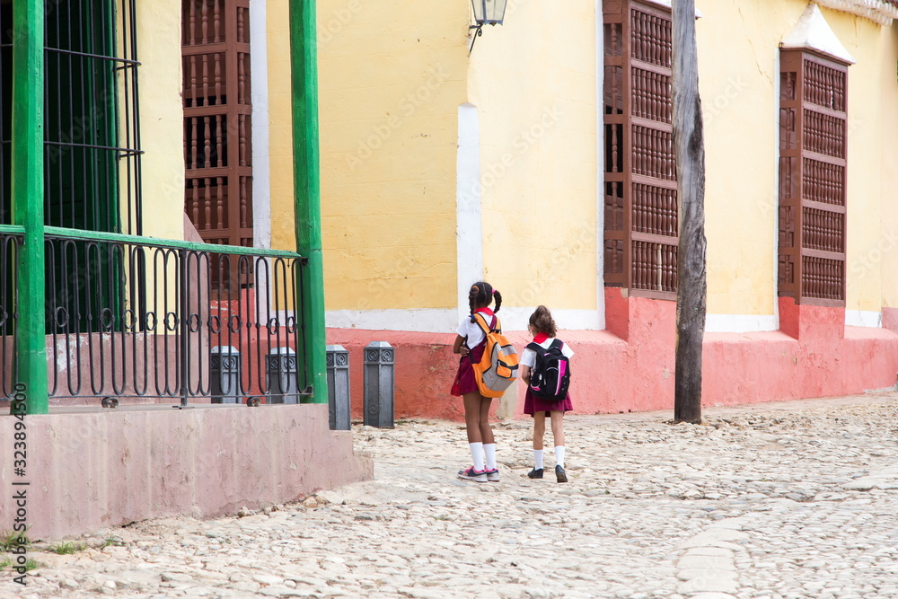 Back view of two small girls in school uniform walking home in old Trinidad, Cuba