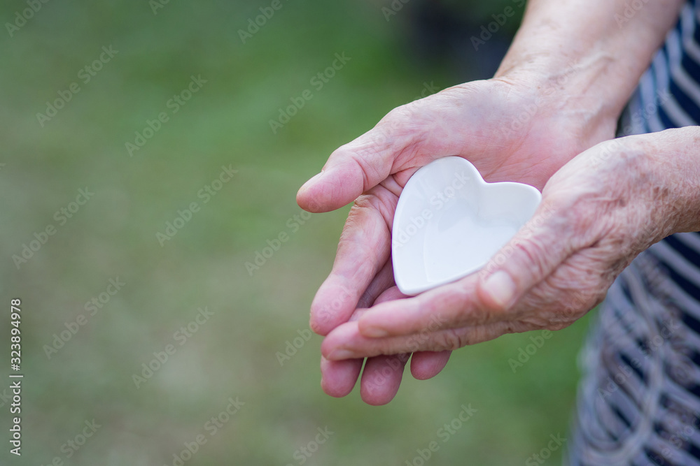 Close-up shot of a heart shaped white ceramic in the hand of an elderly woman. Valentine's day. Heart and Health care concept Close-up shot of a heart shaped white ceramic in the hand of an elderly woman. Valentine's day. Heart and Health care concept