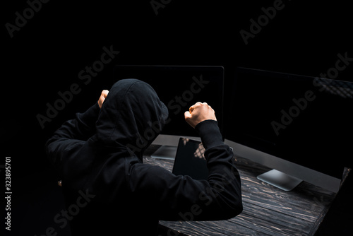 upset hacker with clenched fists near computer monitors with blank screen isolated on black © LIGHTFIELD STUDIOS
