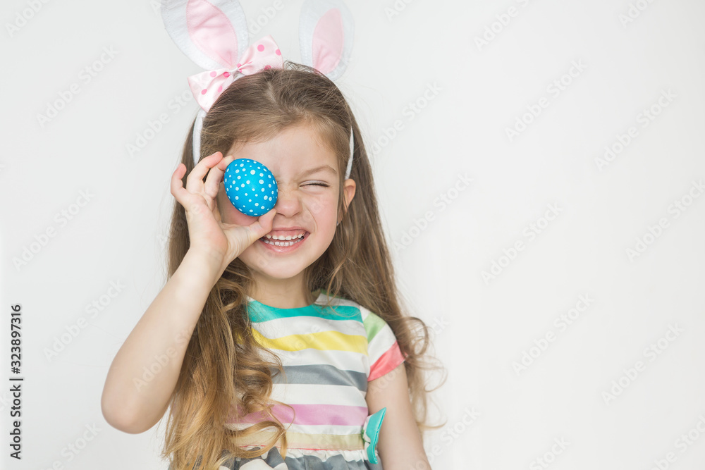 Cute little girl wearing bunny ears and holding painted Easter eggs and smiling on a white background. Easter day.