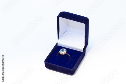 Golden ring with gemstone in a blue jewelry box on white background