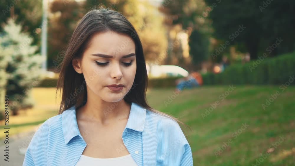 Unhappy girl frawns, being on blurred summer park background. Close up. Copy space. 4K. Unhappy girl frawns, being on blurred summer park background. Close up. Copy space. 4K.