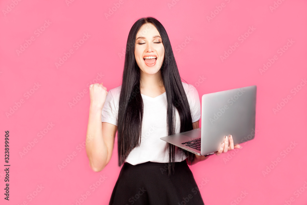 The girl holds a laptop in her hand and smiles, looking up thoughtfully, in a white t-shirt on a pink background. The concept of modern technology or businesswoman. The girl holds a laptop in her hand and smiles, looking up thoughtfully, in a white t-shirt on a pink background. The concept of modern technology or businesswoman.